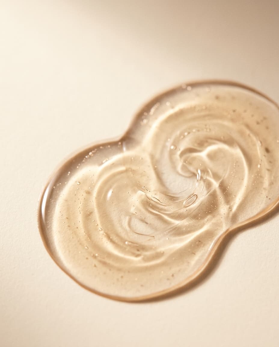 Layered translucent serum texture swirled on a warm cream surface